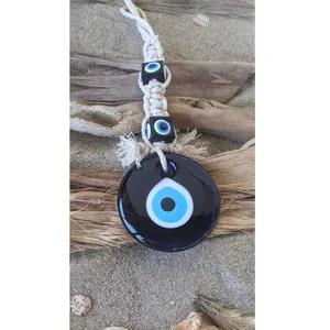 Detail of handmade evil eye macrame pendant with blue glass beads on beach background