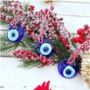 Tre ciondoli Evil Eye in vetro blu appesi a un ramo di pino inneggiato per decorazione