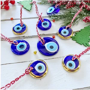 Ornamenti malocchio in vetro blu con bordo dorato e cordoncino rosso su sfondo bianco