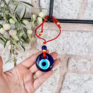 Detail van Turkse Evil Eye hanger in de hand gehouden met rood touw en gouden kralen