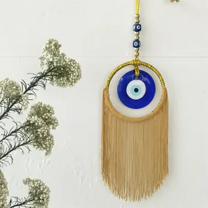 Décoration murale œil turc faite main avec cadre doré et longs pompons beiges sur mur blanc