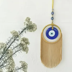 Détail de la tenture murale œil grec bohème avec anneau doré et longs glands beige