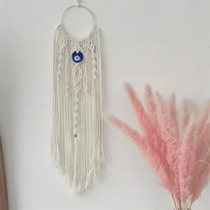 Handmade boho macrame wall hanging with evil eye bead on white plaster wall