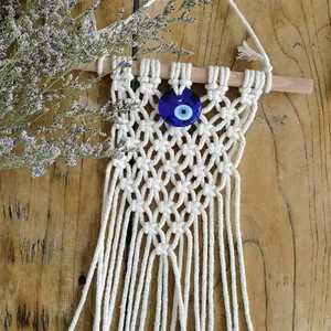 Detail of handmade macramé wall hanging with blue evil eye glass bead and cotton tassels