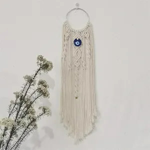 Close-up of hand-woven bohemian wall hanging with cotton rope fringe and evil eye bead