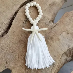 Detail of handmade white wood beads with cotton tassel and starfish on wood background