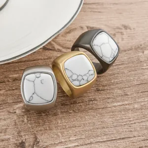 Tres anillos de acero para hombre con piedra de mármol blanco sobre mesa de madera