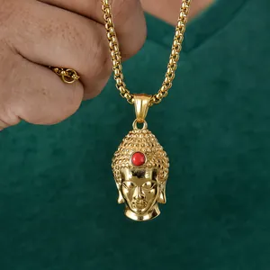 Handheld view of a gold Buddha head pendant necklace with red stone on green background