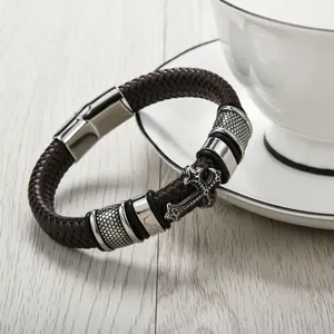 Gros plan du bracelet en cuir tressé marron foncé avec détail de croix en acier argenté