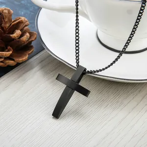 Minimalistische schwarze Edelstahl-Kreuzkette auf rustikaler Holzfläche mit Deko