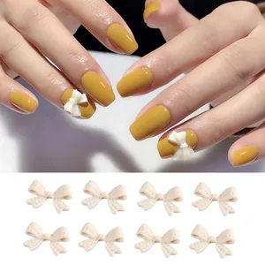 Dettaglio di fiocchi in resina opaca color crema per nail art applicati su unghie gialle