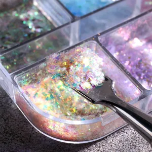 Makro-Detail von irisierenden Aurora-Opal-Nagelflocken, die mit einem Metalltool aufgenommen werden