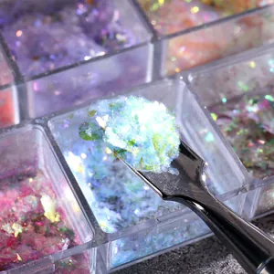 Makroaufnahme von irisierenden Aurora Opal-Flocken in Blau auf einem kleinen Nagellöffel