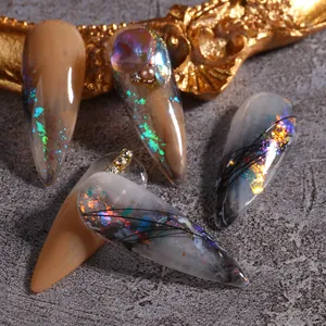 Macro shot of long stiletto press-on nails with marble texture, aurora foil and 3D jewels