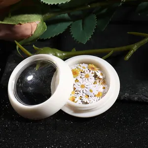 Macro shot of white and yellow daisy nail art flakes in premium round jars on black rock
