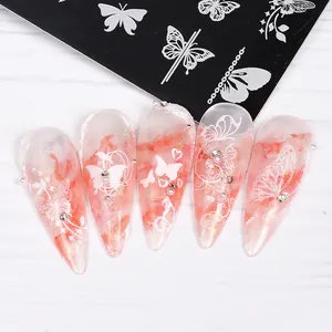 Detail of red marble stiletto nails with white butterfly patterns and metal stamping plate