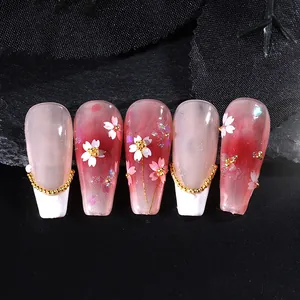 Dettaglio di unghie finte sfumate rosa e bordeaux con fiori di ciliegio e tocchi dorati