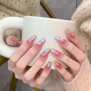 Primer plano de uñas largas bailarina con degradado rojo y fragmentos de concha