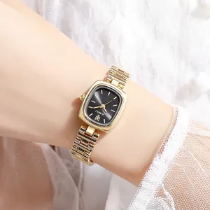 Montre élégante en métal doré avec cadran noir carré portée sur fond de dentelle