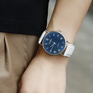 Close-up of blue Roman numeral dial and silver alloy case on a white leather watch strap