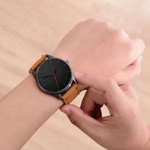 Close-up of minimalist black dial watch with red second hand and brown leather strap