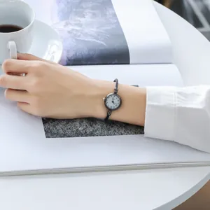 Close-up of a minimalist black bracelet watch with a white dial on a woman's wrist