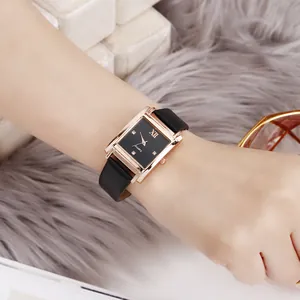 Rechteckige roségoldene Uhr mit schwarzem Lederarmband getragen auf Plüschhintergrund
