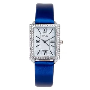 Close-up of rectangular silver watch with crystal bezel and blue satin leather strap