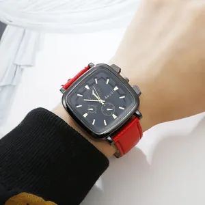 Close-up of square black dial watch with gold indices and red leather strap on wrist