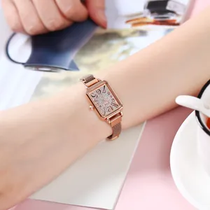 Women's rose gold rectangular watch with crystal bezel and mesh band on a wrist
