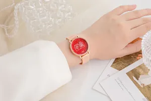 Dettaglio dell'orologio con cinturino a maglia oro rosa e quadrante rosso con scritte
