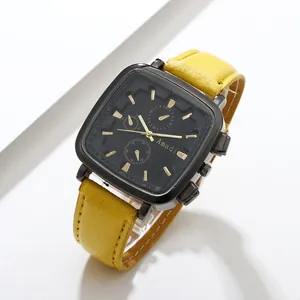 Detail of square black watch dial with golden hands and bright yellow leather strap
