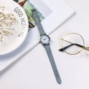 Minimalist small dial women's watch with grey leather strap on a white table