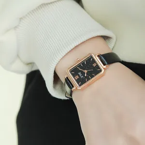 Women's watch with rectangular rose gold case and black leather strap worn on wrist
