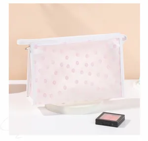 Détail d'une trousse à maquillage en filet avec fleurs roses, poignée et zip métallique