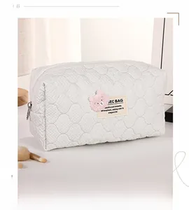 Detailed view of white quilted cosmetic bag featuring pink bear embroidery and soft fabric