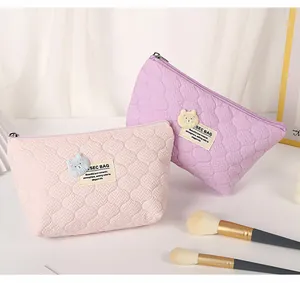 Detailed texture of quilted cream-style makeup bags with cute bear patches in pink and purple