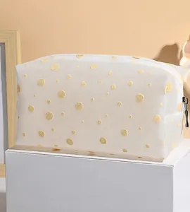 Détail de la trousse à maquillage en maille blanche à pois jaunes sur un support