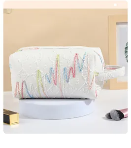 Dettaglio della borsa da trucco bianca con ricamo a onde colorate e manico laterale