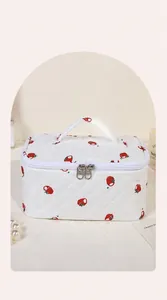 Detail van witte gewatteerde make-uptas met rode fruitprint en grote opening handvat