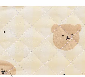 Close-up of quilted beige fabric with cute bear pattern and diamond stitching detail