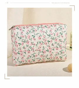 Detailopname van een witte gewatteerde make-uptas met bloemenprint en roze ritssluiting