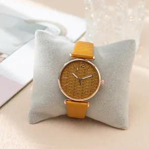 Close-up of mustard yellow leather watch with embossed leaf dial on velvet pillow