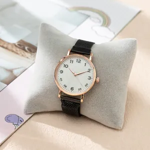 Close-up of rose gold quartz watch with black mesh strap on a grey pillow