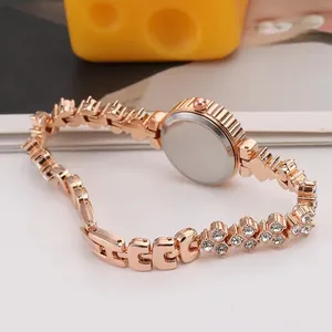 Dettaglio orologio oro rosa con cinturino in metallo a maglie H e strass su un tavolo