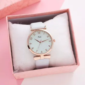 Detail of rose gold quartz watch with white leather strap and a bow charm in a gift box