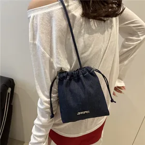 Borsa a secchiello in denim blu scuro con coulisse, indossata a tracolla per un look casual