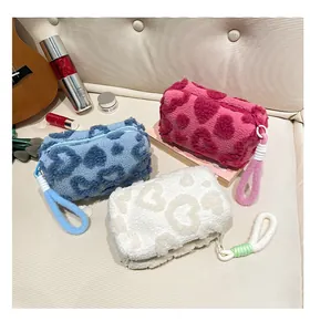 Three plush heart-pattern cosmetic bags in blue, pink, and white with handles