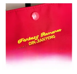 Close-up of red fabric handbag with yellow embroidery and pink snap button closure