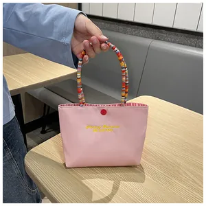 Detailed view of pink handbag with 'Fantasy Romance' embroidery and colorful beaded handle